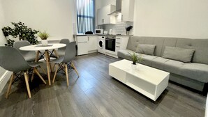A modern kitchen with white cabinets, a dining area with a round table and chairs, and a grey sofa. - Albert Luxury Hottub and Jacuzzi Apartments (Blackpool)