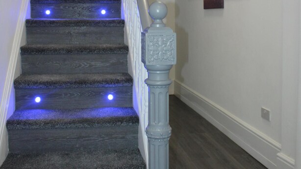 A staircase with blue LED lights, a white balustrade, and a wall with three framed pictures. - Albert Luxury Hottub and Jacuzzi Apartments (Blackpool)