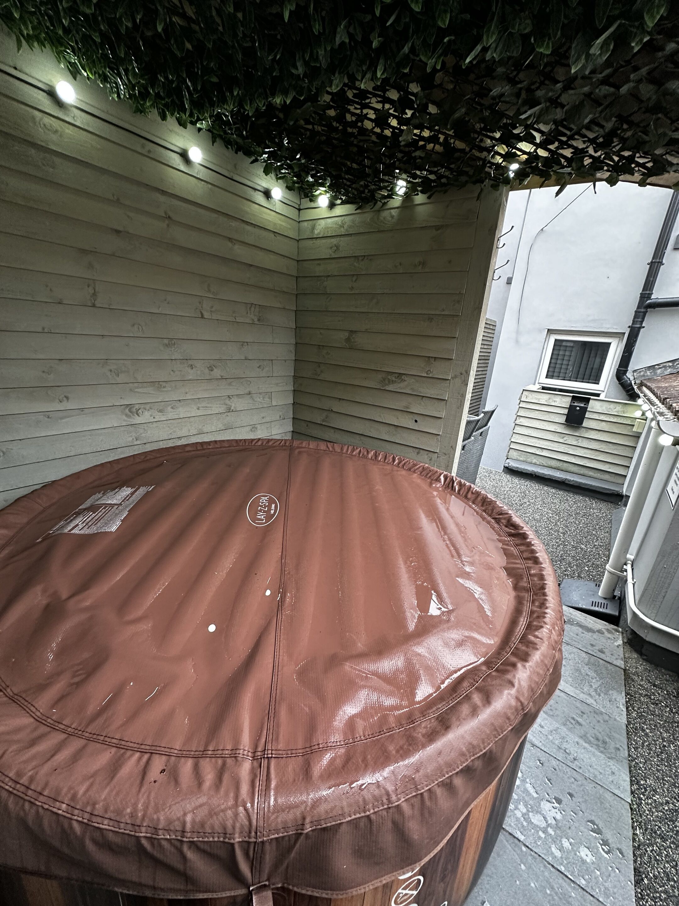 A hot tub with a brown cover, surrounded by wooden walls and a ceiling with hanging plants.