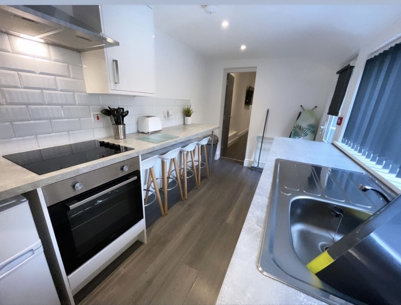 A modern kitchen with a built-in oven, a stainless steel sink, and a bar stool area.