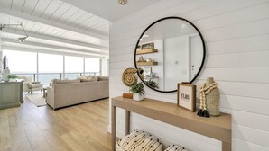 Een moderne woonkamer met een groot raam, een ronde spiegel, een console met decoratieve objecten en een beige bank.