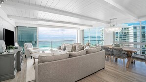 Een moderne woonkamer met een grote bank, een eettafel en stoelen, met uitzicht op een stadsbeeld en de oceaan.