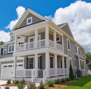 A two-story residential building with a front porch, multiple windows, and a garage. - Coastal Club * 5BR Luxury Beach House (LEWES)