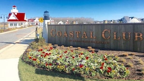 Señal de Coastal Club con una señal de límite de velocidad de 25 millas por hora, un faro y un jardín de flores al frente.