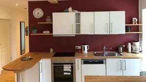 A modern kitchen with white cabinets, a wooden countertop, a built-in oven, a dishwasher, and a red accent wall. - Ferienwohnung Oma Rosa mit Traumblick und Zentrumsnähe (Berchtesgaden)