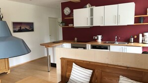 A modern kitchen with white cabinets, a wooden countertop, and a built-in dishwasher. There is a clock on the wall and a plant on the countertop. - Ferienwohnung Oma Rosa mit Traumblick und Zentrumsnähe (Berchtesgaden)