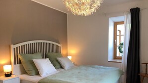 A neatly arranged bedroom with a bed, bedside tables, a lamp, a window with curtains, and a hanging light fixture. - Ferienwohnung Oma Rosa mit Traumblick und Zentrumsnähe (Berchtesgaden)