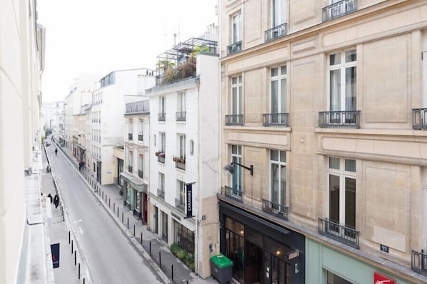A narrow urban street lined with multi-story buildings, featuring balconies and storefronts.