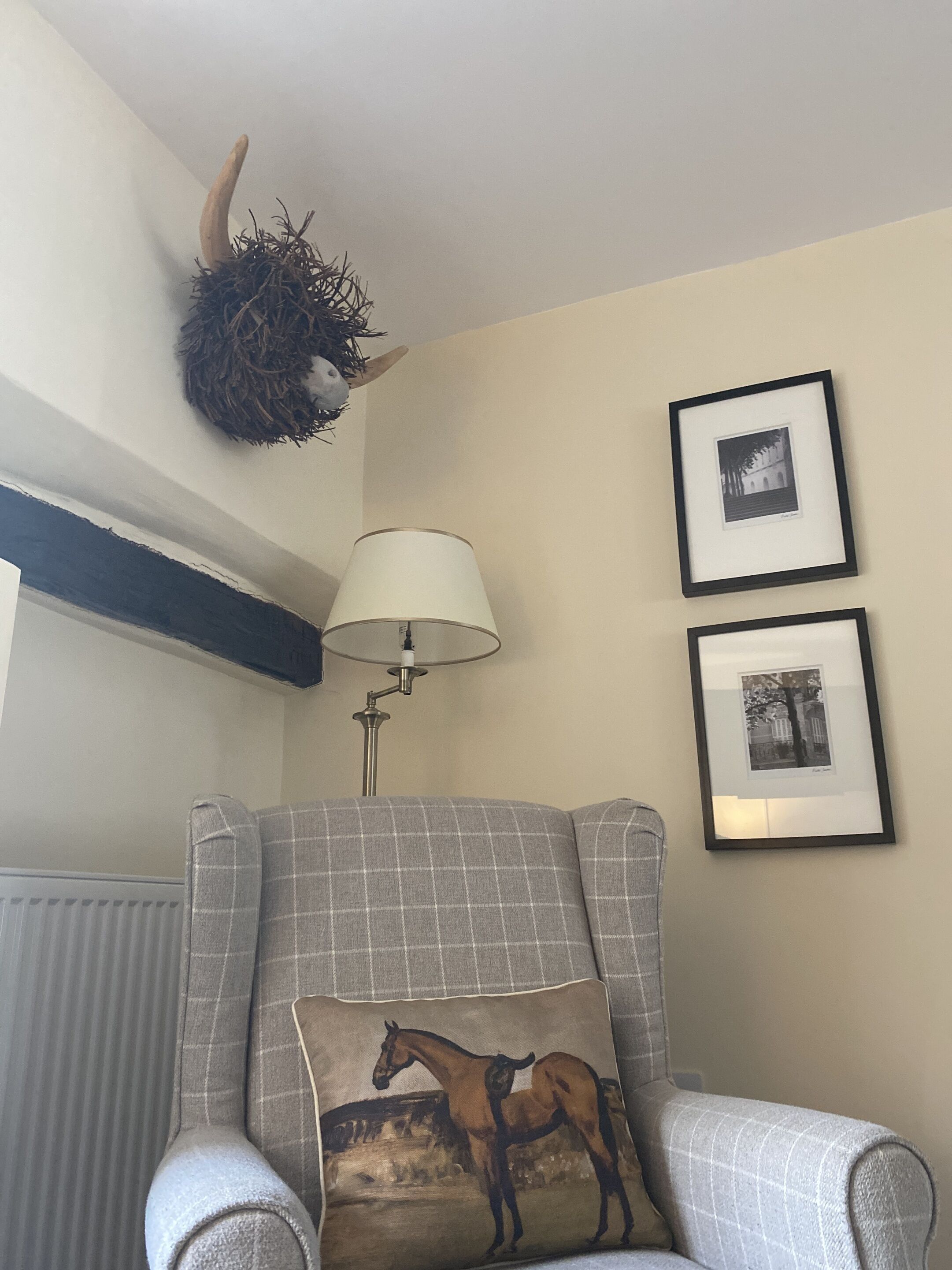 Ein Zimmer mit einem grauen Sessel, einer Lampe, einem an der Wand befestigten Horn und zwei gerahmten Bildern.