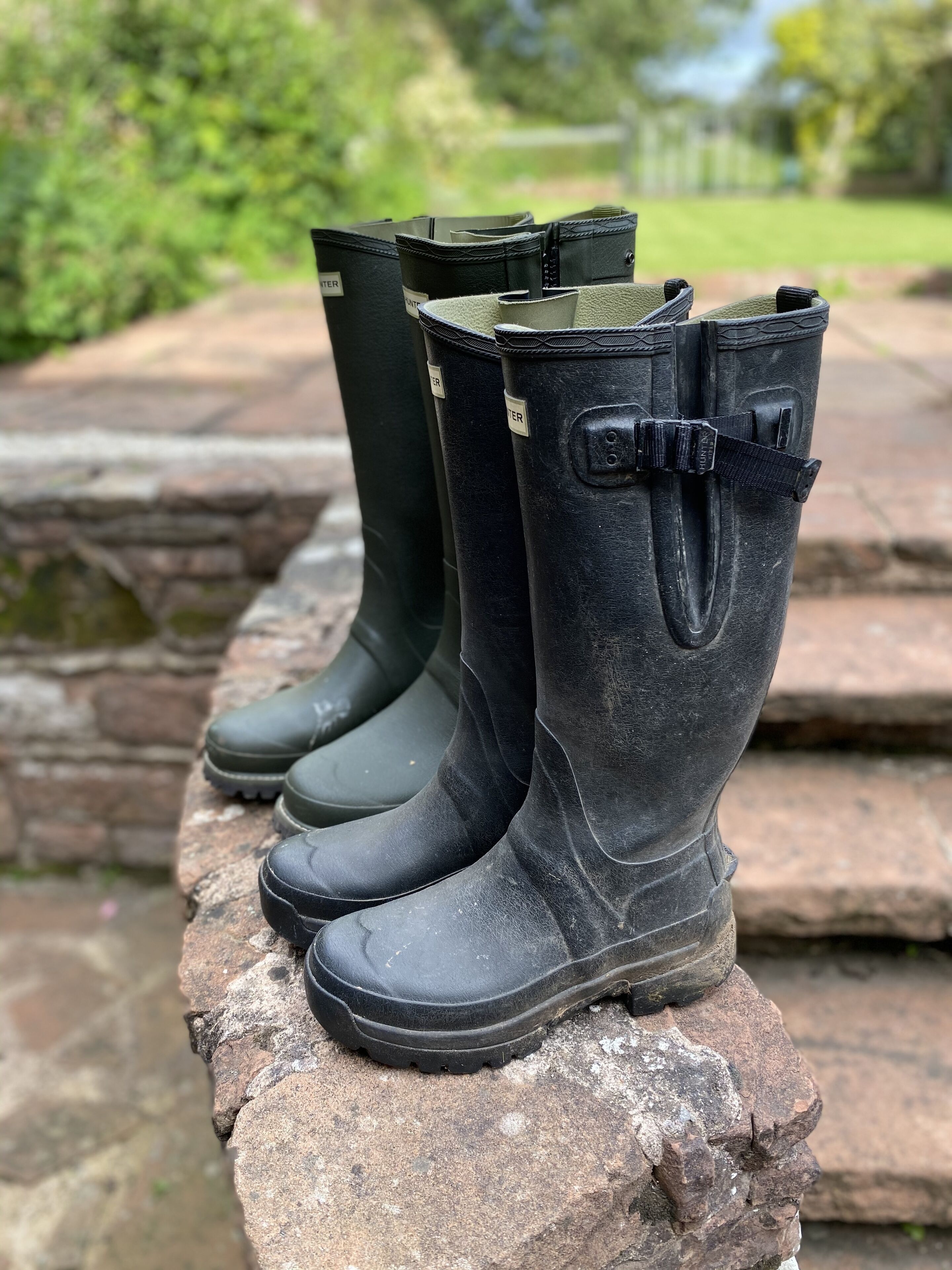 A pair of black rubber boots with a strap and buckle, placed on a stone ledge.