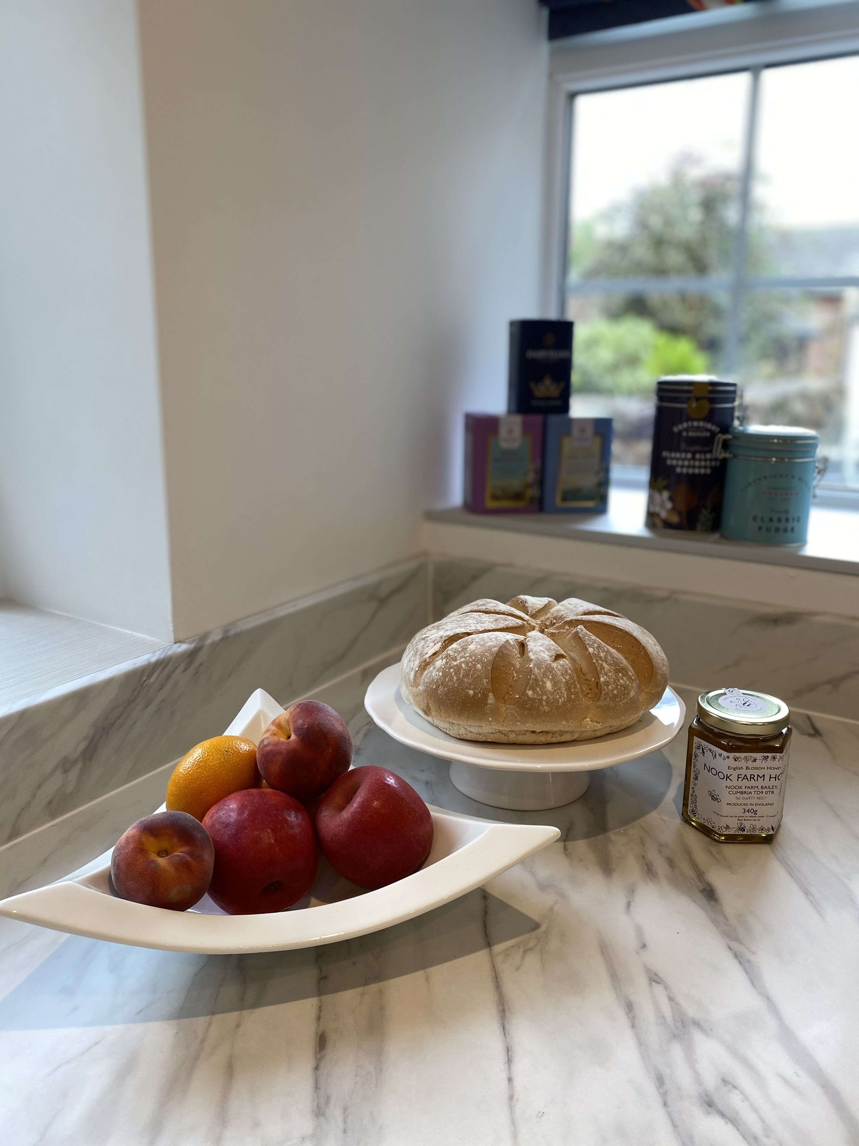 A kitchen counter with a loaf of bread, a plate of fruit, and a honey jar.