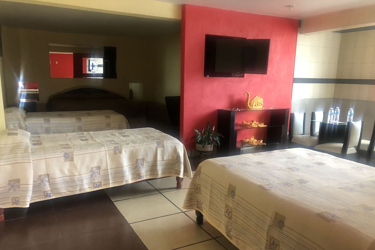 A hotel room with two beds, a TV mounted on the wall, a red accent wall, a small plant, and a water dispenser.