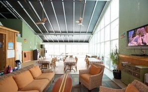 A spacious indoor area with a high ceiling, large windows, and a television on the wall. - Two Bedroom Ocean View Condo, Myrtle Beach (2027817) (North Myrtle Beach)