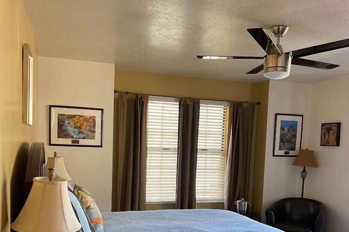 A hotel room with a bed, a desk with a lamp, a chair, and a ceiling fan.