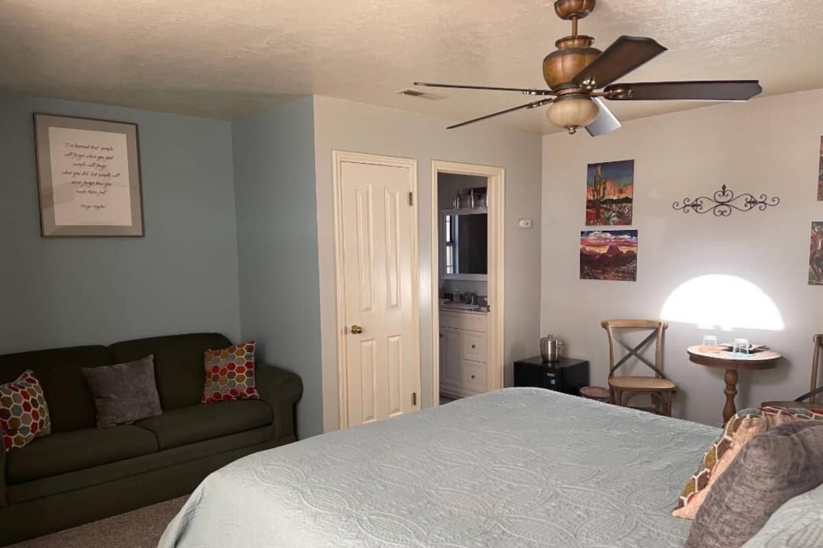 A bedroom with a bed, a ceiling fan, a dresser, a chair, and a desk with a lamp.