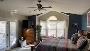 A bedroom with a bed, dresser, TV, and a ceiling fan. - Harvest House Inn (Springdale)