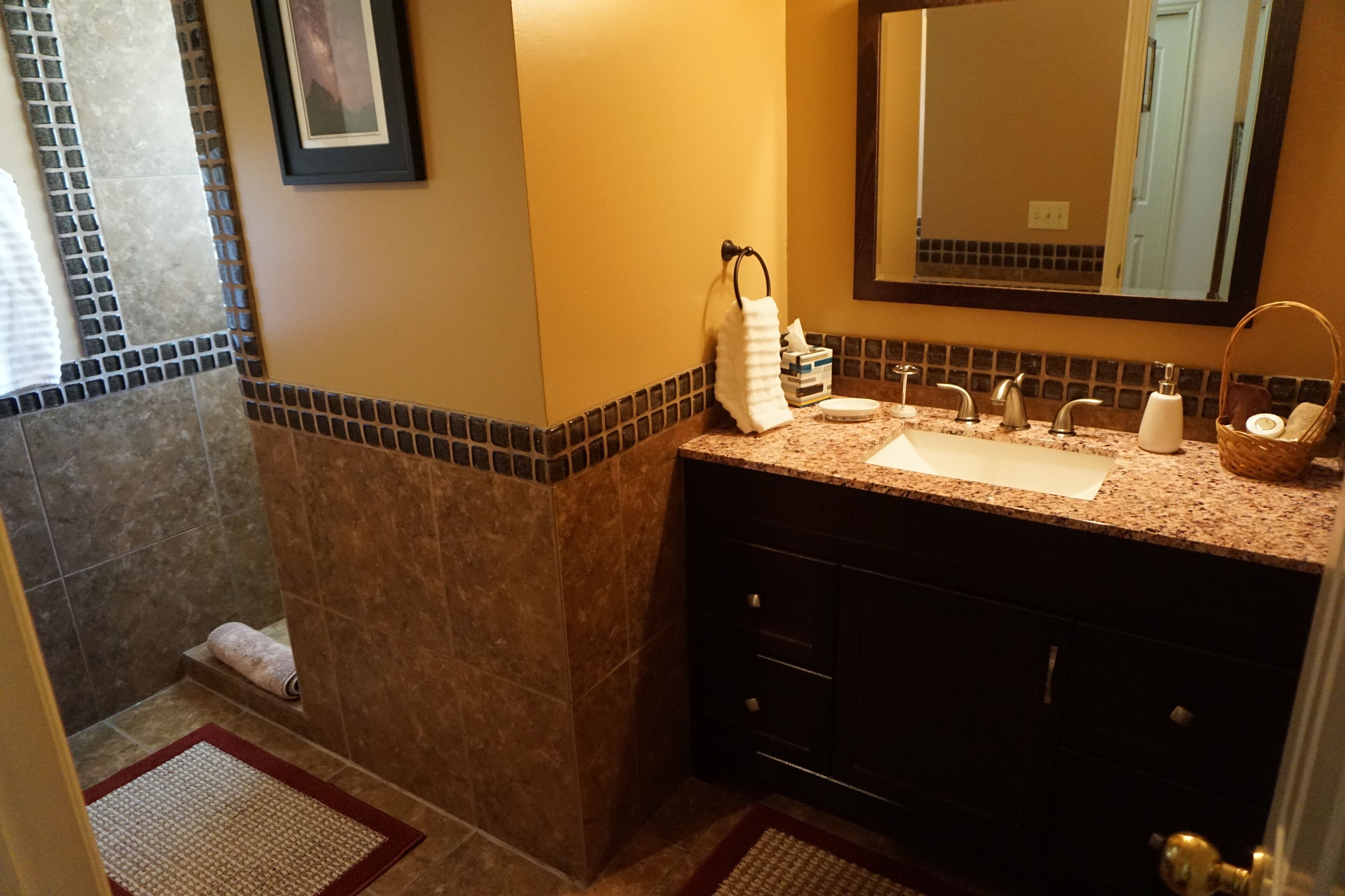 Un baño con encimera de granito, un lavabo, un espejo y un perchero para toallas.