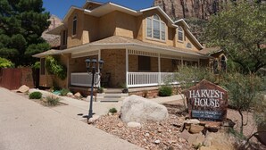 A two-story house with a porch, a sign indicating it is a harvest house offering bed and breakfast, and a view of a rocky mountain in the background. - Harvest House Inn (Springdale)