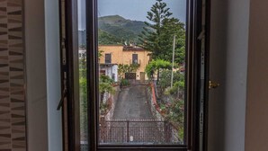 Une vue à travers une fenêtre sur une rue étroite bordée d’immeubles, avec une porte et une montagne en arrière-plan.
