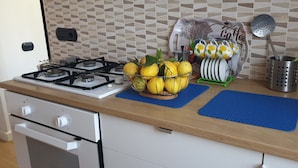Une cuisine équipée d’une cuisinière à gaz, d’un panier de fruits, d’un égouttoir et d’un évier.