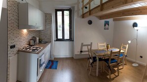 Une cuisine compacte équipée d’une cuisinière, d’un évier et de placards, un coin repas avec une table et des chaises, et une chambre en mezzanine avec un plafond en bois.