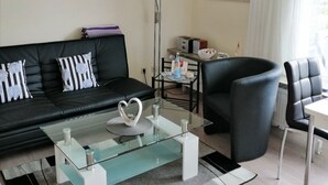 Ein modernes Wohnzimmer mit einem schwarzen Ledersofa, einem Glastisch mit einer weißen Schwanenfigur, einem schwarzen Sessel und einem weißen Tisch.