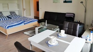 Ein Schlafzimmer mit einem Bett, einem schwarzen Sofa, einem Glastisch mit zwei weißen Tassen sowie einem Schreibtisch und einem Stuhl.