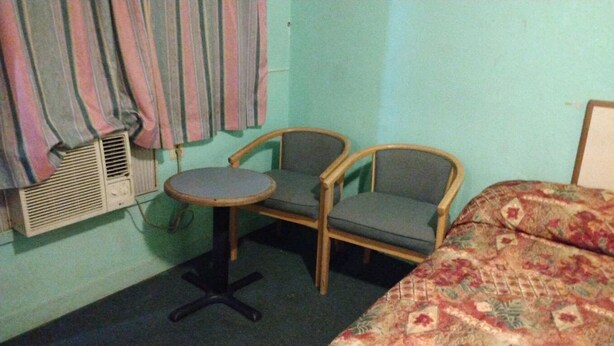 A room with a bed, two chairs, a small round table, and a wall-mounted heater.
