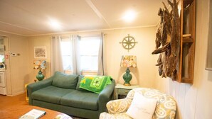 A living room with a green sofa, a patterned armchair, a wooden coffee table, and a wall-mounted decorative piece. - Lakeside property. Private dock. Great for ANO! (Russellville)