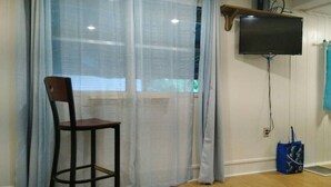 A room with a wooden floor, a chair, a TV mounted on the wall, and a window with sheer curtains. - Lakeside property. Private dock. Great for ANO! (Russellville)