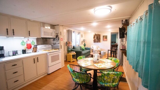 A compact kitchen with white cabinets, a microwave, and a stove. There is a dining area with a table and chairs, and a living area with a couch and a TV. - Lakeside property. Private dock. Great for ANO! (Russellville)