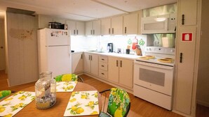 A compact kitchen with white cabinets, a microwave, a stove, and a refrigerator. There is a dining table with chairs and a glass jar on it. - Lakeside property. Private dock. Great for ANO! (Russellville)