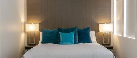 A neatly made bed with a white quilt, two side tables with lamps, and a wooden headboard.