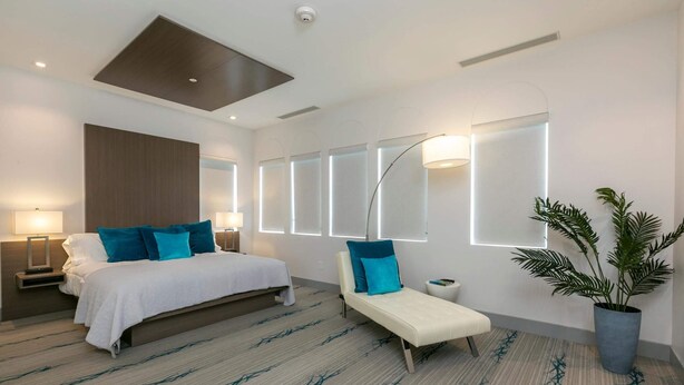 A modern hotel room with a large bed, bedside tables, a sofa, and a potted plant. - 2 Bedroom, Sleeps 6 Guests (Cruz Bay)