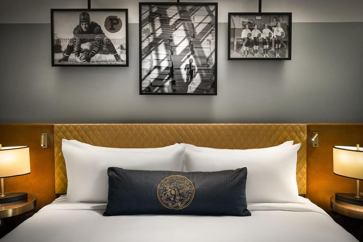 Una habitación de hotel con una cama, dos lámparas de noche, un cabecero y tres cuadros en la pared.