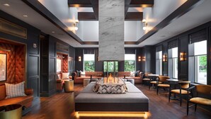 A modern lounge area with a central seating area, wooden flooring, and large windows providing natural light. - The Union Club Hotel at Purdue University, Autograph Collection (West Lafayette)
