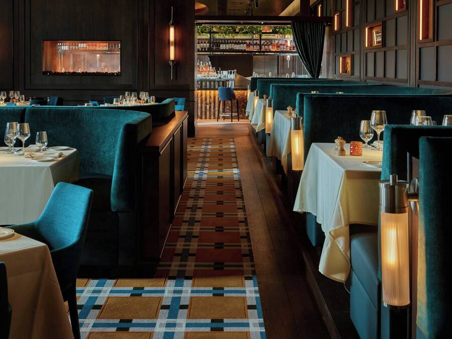 Un restaurante con cabinas y mesas, una alfombra estampada y una zona de bar al fondo.