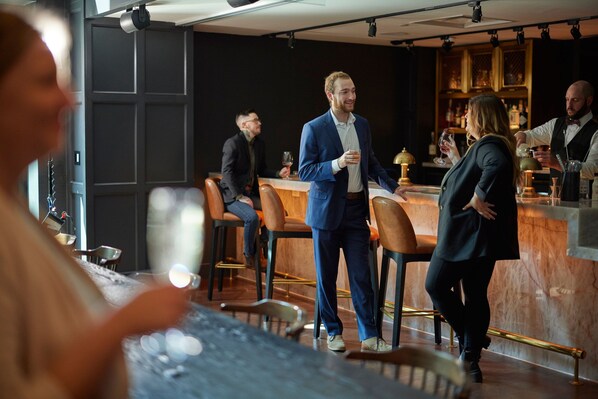 A bar area with wooden chairs, a marble counter, and a bartender.