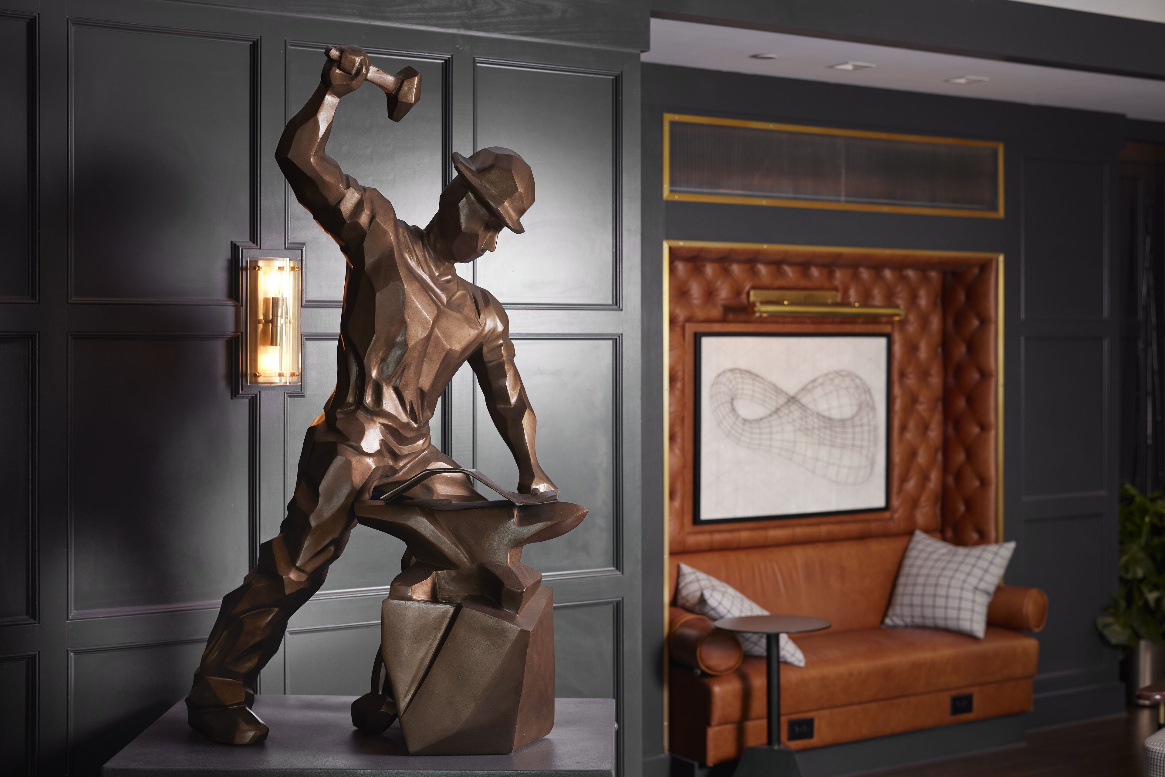 A bronze statue of a man in a dynamic pose, a leather sofa, and a framed abstract artwork in a modern interior.