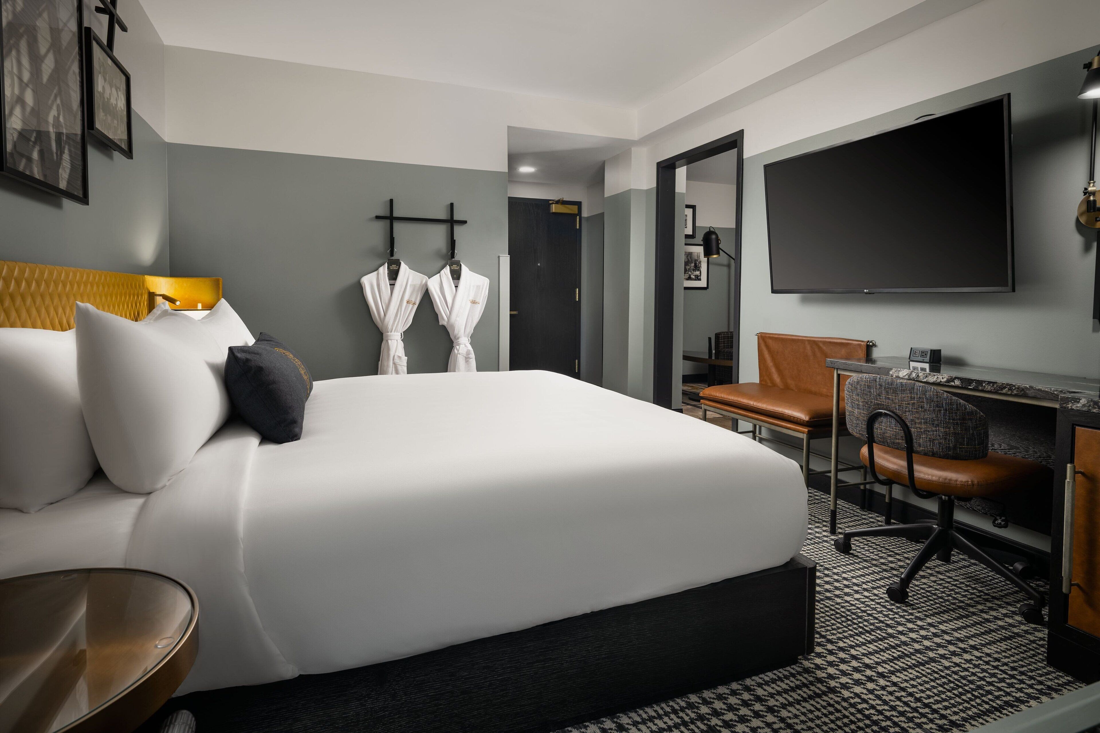 Habitación de hotel con una cama grande, un escritorio con silla, un televisor y dos batas colgadas en ganchos.