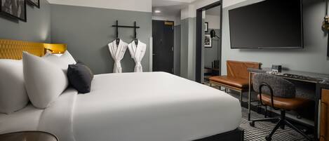 Habitación de hotel con una cama grande, un escritorio con silla, un televisor y dos batas colgadas en ganchos.