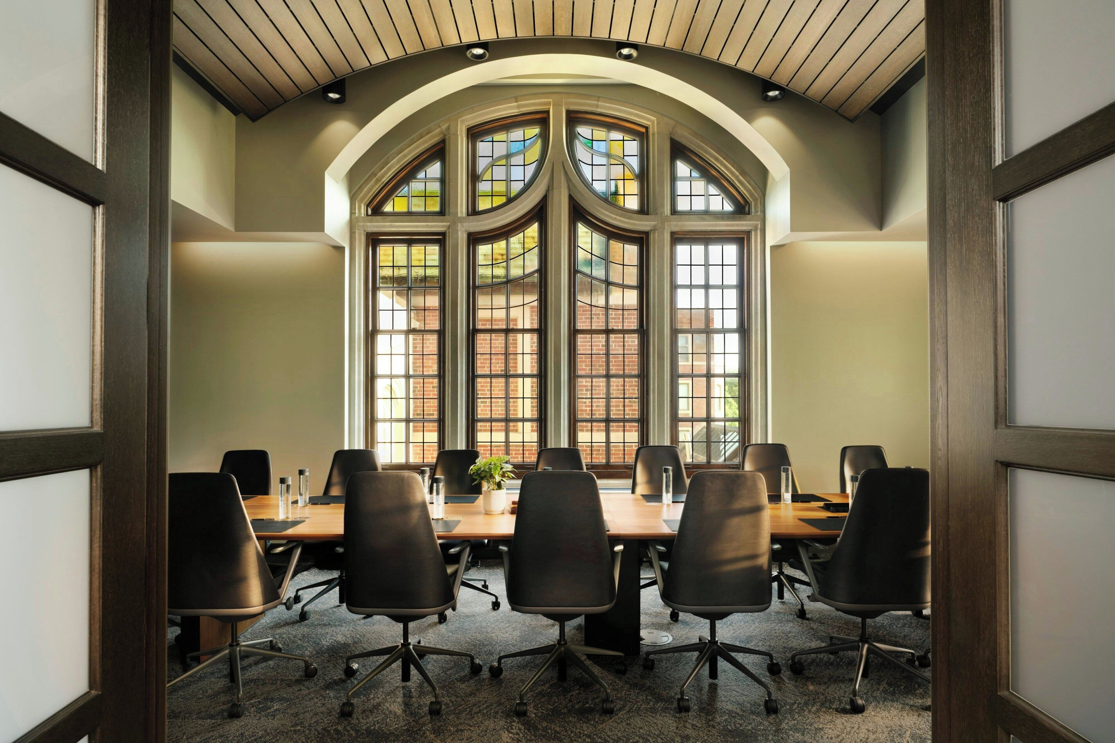 Une salle de conférence avec une longue table, six chaises et de grandes fenêtres donnant sur des immeubles en briques.