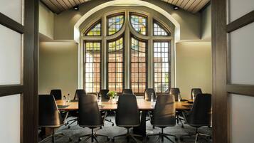 Une salle de conférence avec une longue table, six chaises et de grandes fenêtres donnant sur des immeubles en briques.