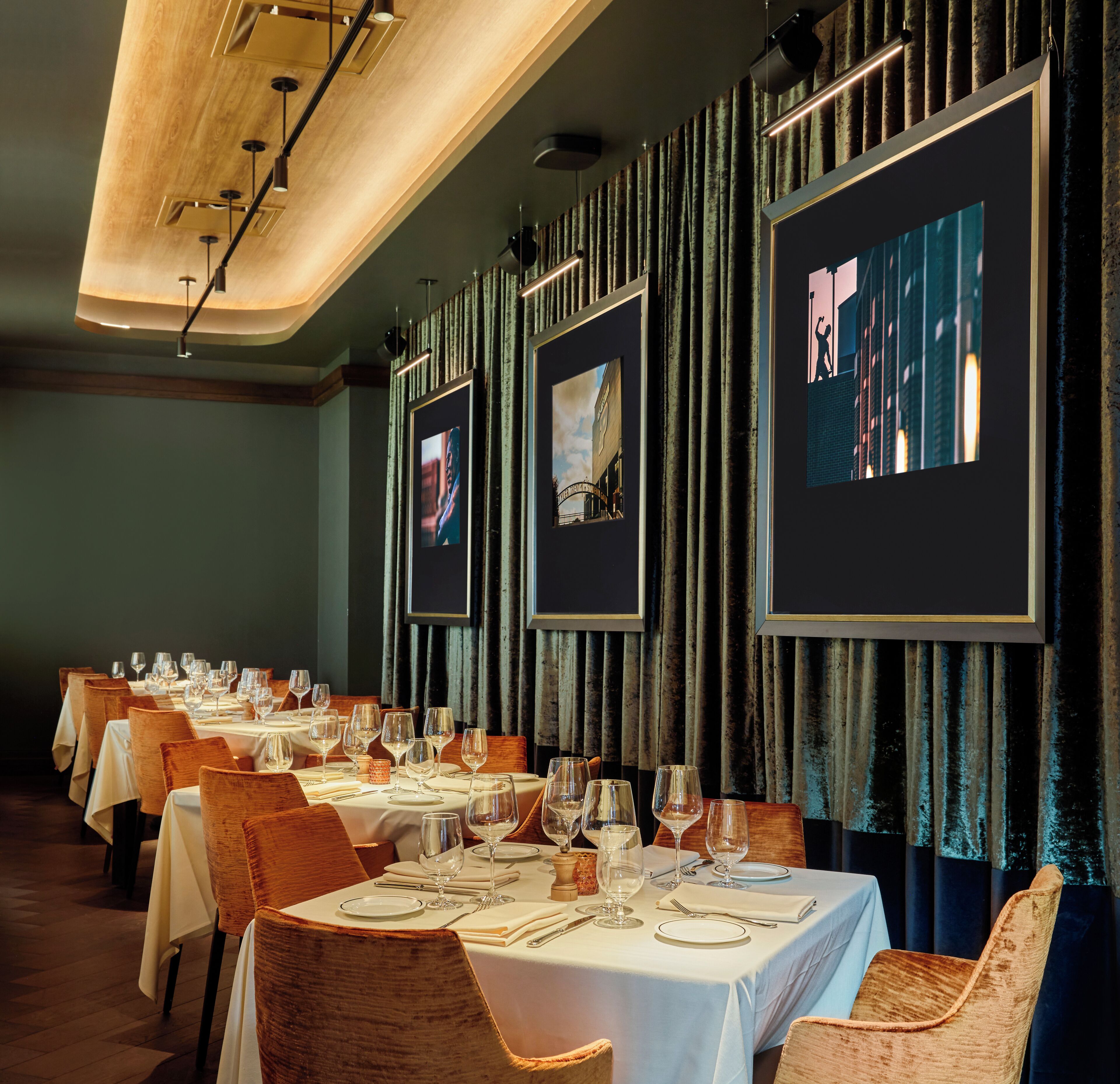 Un restaurant doté de nombreuses tables dressées pour le service, avec un intérieur moderne agrémenté de rideaux sombres et d’œuvres d’art encadrées aux murs.