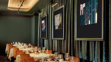 Un restaurant doté de nombreuses tables dressées pour le service, avec un intérieur moderne agrémenté de rideaux sombres et d’œuvres d’art encadrées aux murs.