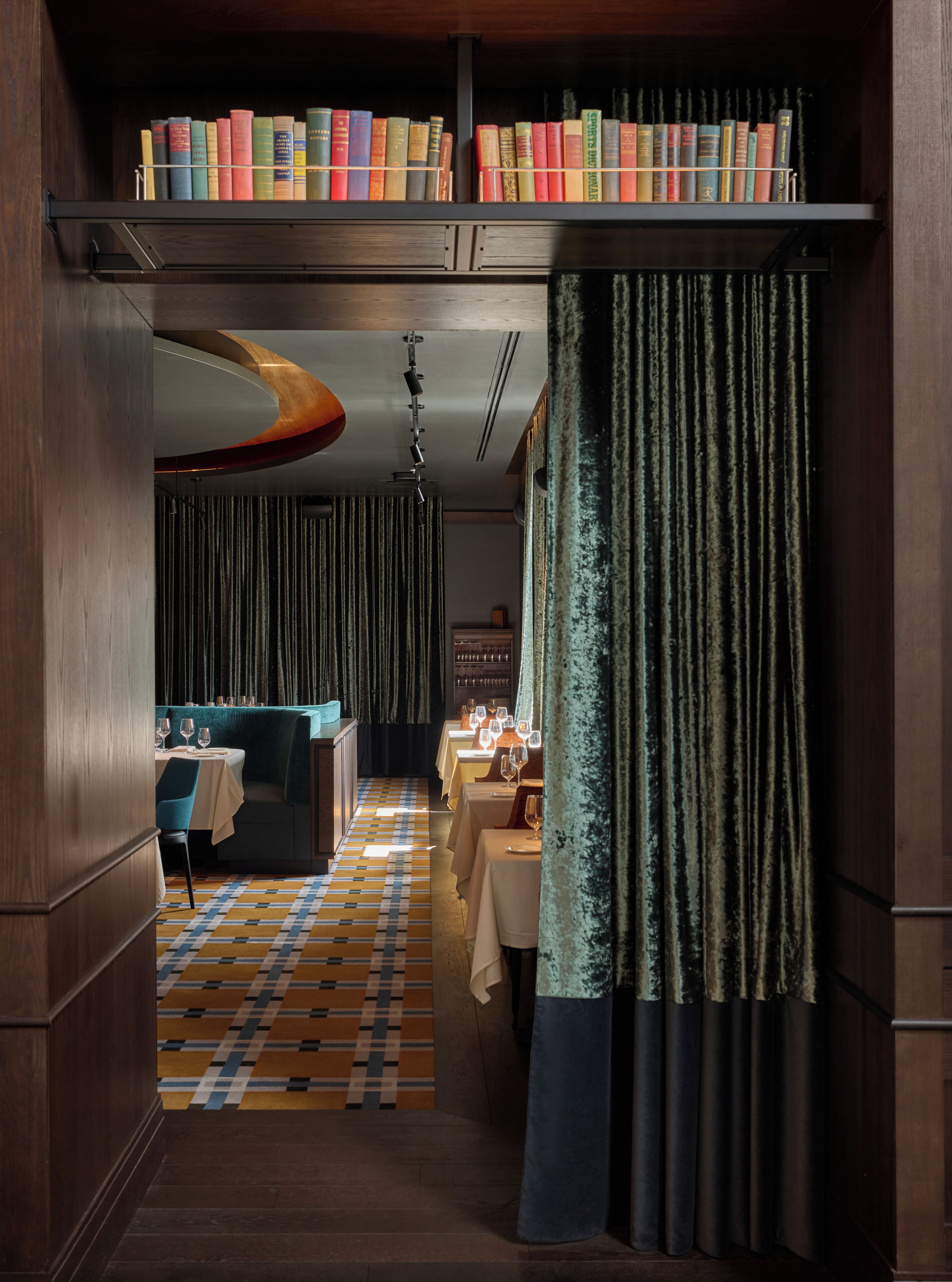 Un vestíbulo de hotel con suelo a cuadros, una zona de bar y una estantería llena de libros.