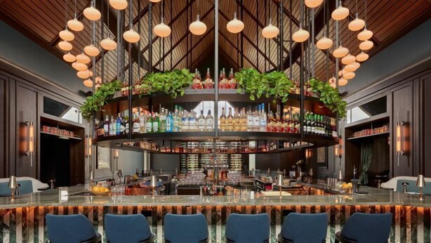 A bar area with a curved ceiling, hanging pendant lights, and a bar counter with stools. - The Union Club Hotel at Purdue University, Autograph Collection (West Lafayette)