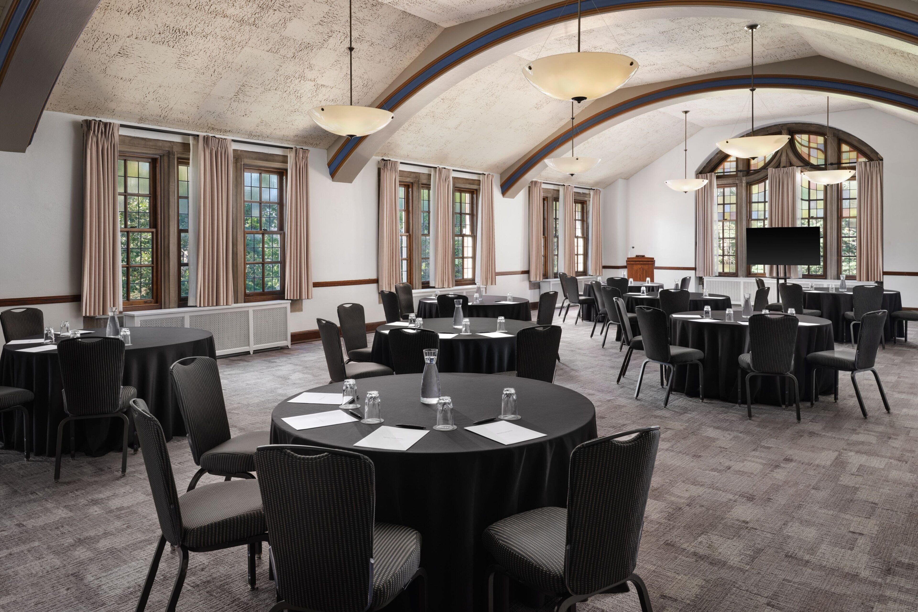 A conference room with round tables, chairs, and a large screen.