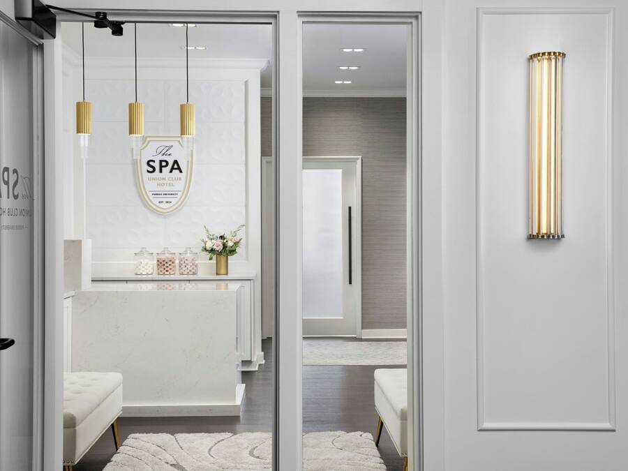 Un spa moderno con tocador blanco, espejo con marco dorado y un jarrón decorativo con flores.