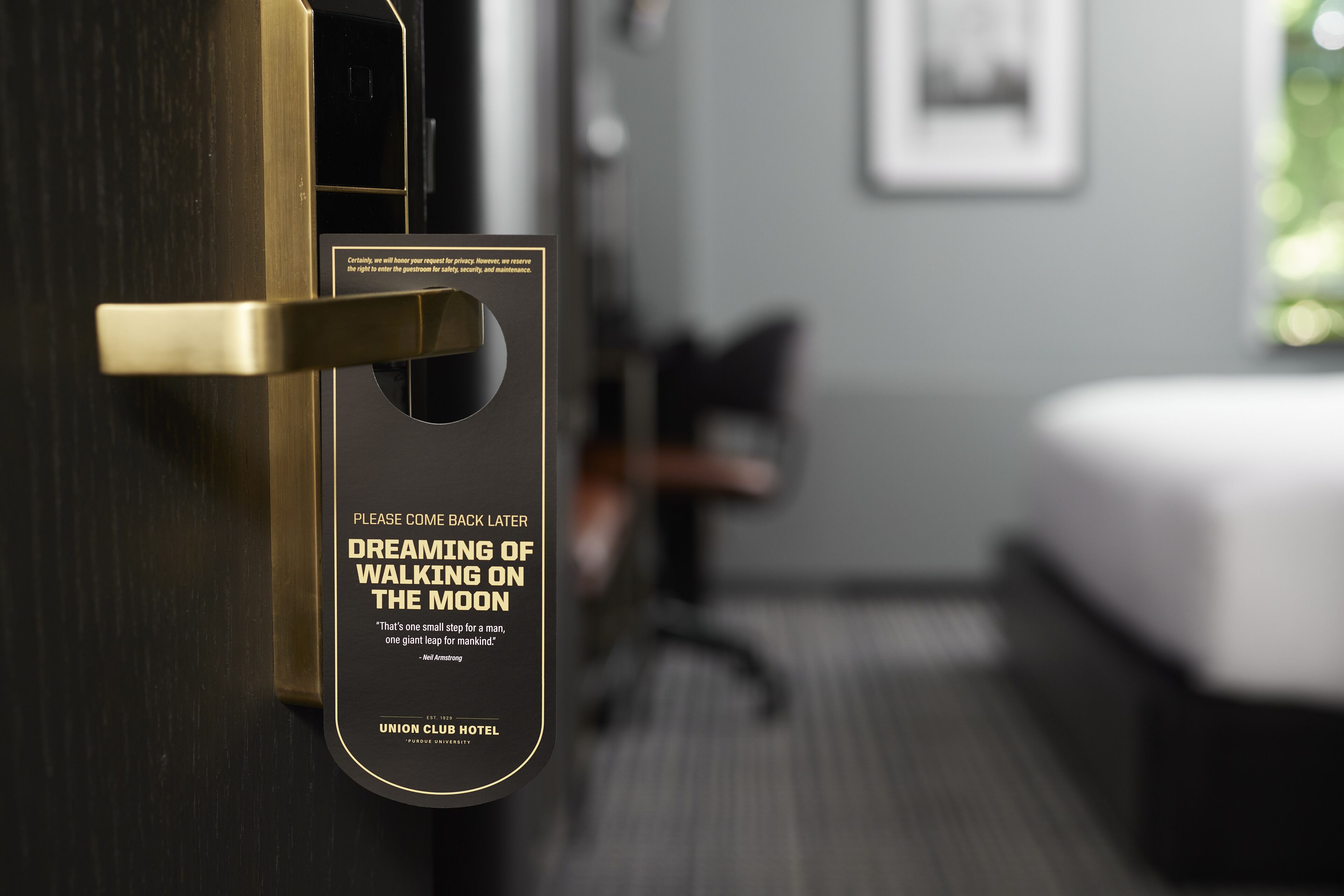 A hotel room with a door featuring a sign that reads "Please come back later" and "Dreaming of walking on the moon."